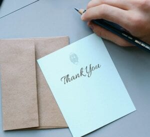 Paper with THANK YOU written on it and envelope with a hand holding a pencil