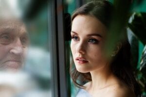 Woman looking into a reflection of an older woman looking back at her in a window.