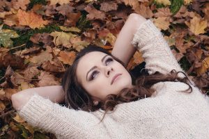 Brunette woman laying on a bed of colorful leaves looking into the sky above.