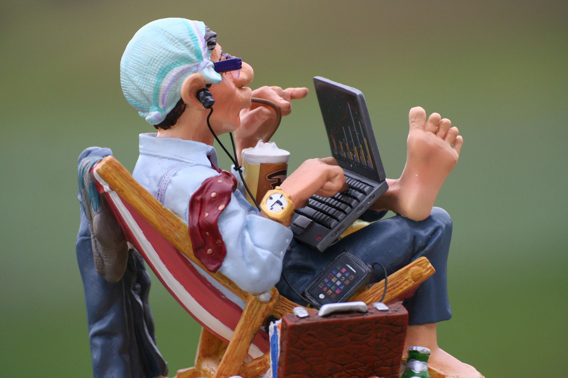 Claymation figure of a man sitting in a lounge chair barefoot while working on a laptop computer.