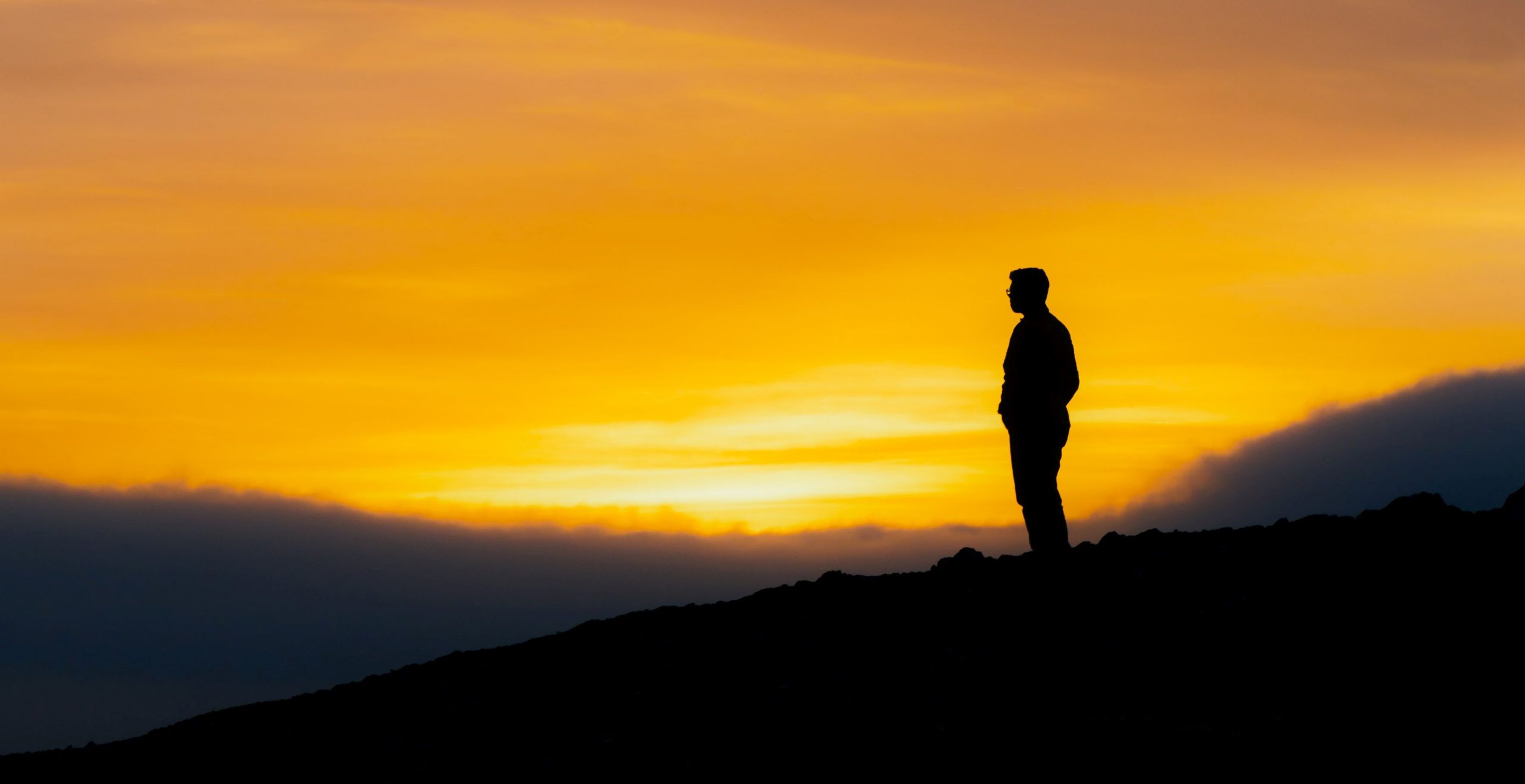 Silhouette of a man standing against a sunset backdrop.